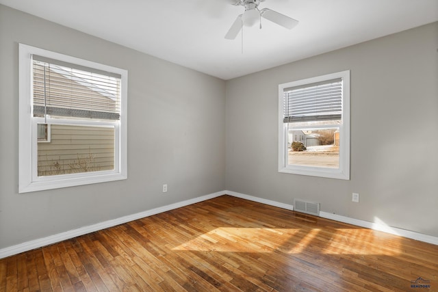 empty room featuring ceiling fan, visible vents, baseboards, and hardwood / wood-style floors