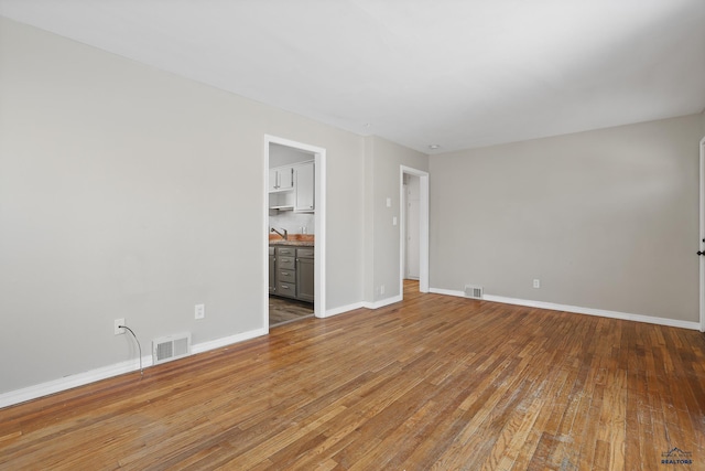 empty room with light wood-type flooring, visible vents, baseboards, and a sink