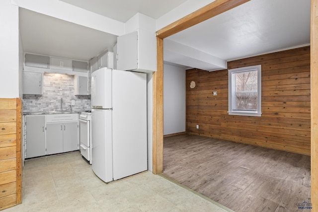 kitchen featuring backsplash, wood walls, light countertops, white appliances, and a sink