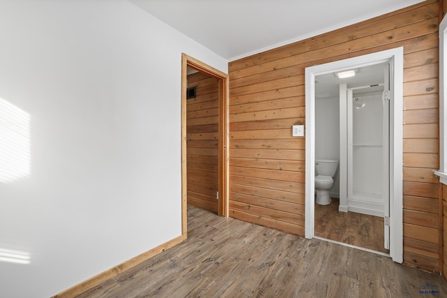 unfurnished bedroom featuring wooden walls, ensuite bath, and wood finished floors