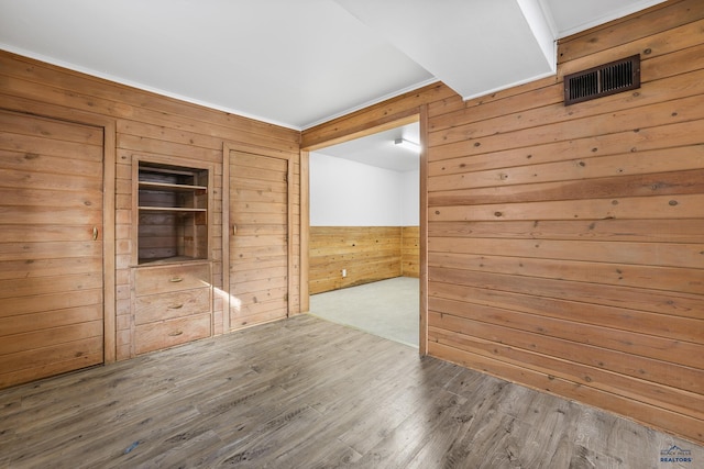 unfurnished room with visible vents, wood walls, and wood finished floors