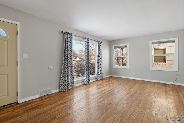 empty room with hardwood / wood-style floors, baseboards, and visible vents