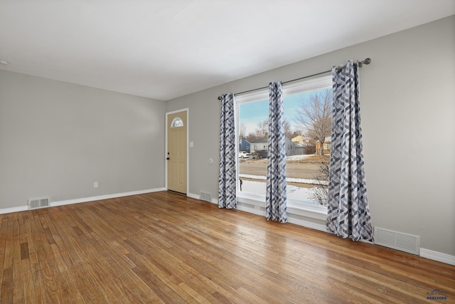 unfurnished room featuring visible vents, baseboards, and hardwood / wood-style floors