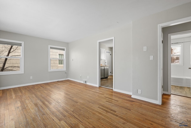 unfurnished bedroom with hardwood / wood-style floors, visible vents, baseboards, and connected bathroom