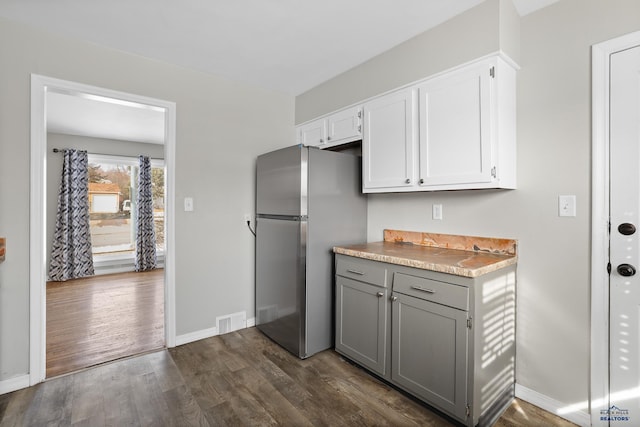 kitchen featuring visible vents, gray cabinetry, dark wood-type flooring, freestanding refrigerator, and white cabinets