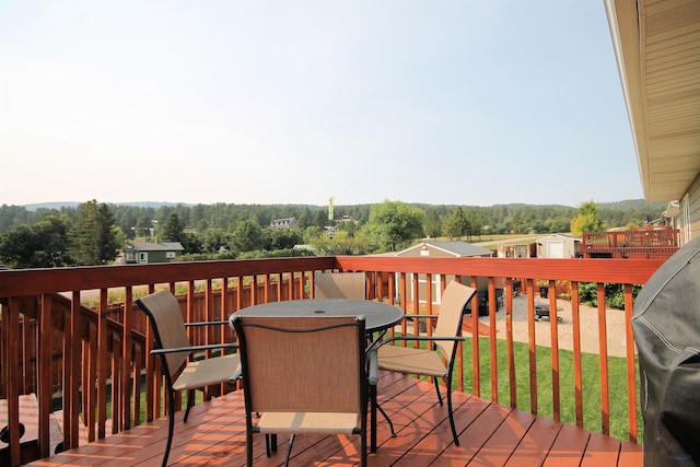 wooden deck featuring outdoor dining area, a lawn, and a wooded view