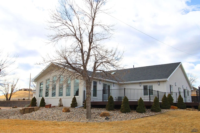 exterior space with stucco siding, a wooden deck, a front lawn, and a shingled roof