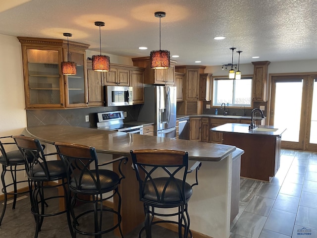 kitchen featuring backsplash, brown cabinets, appliances with stainless steel finishes, a peninsula, and a sink