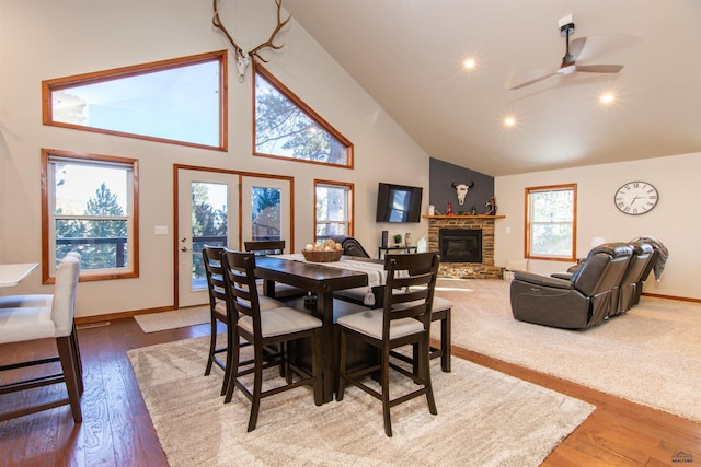 dining space featuring baseboards, wood-type flooring, high vaulted ceiling, and a glass covered fireplace