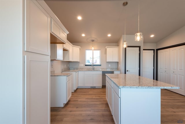 kitchen with a center island, light stone countertops, recessed lighting, wood finished floors, and a sink