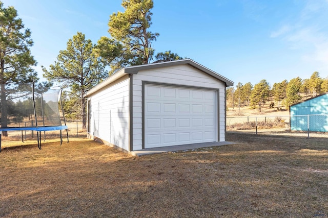 detached garage featuring a trampoline, fence, and driveway