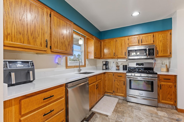 kitchen with brown cabinetry, appliances with stainless steel finishes, light countertops, and a sink