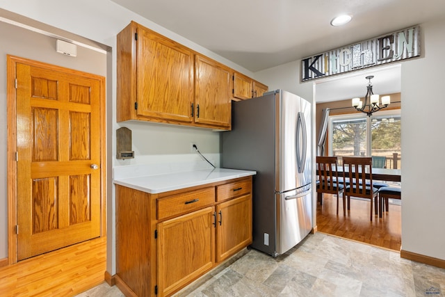 kitchen with freestanding refrigerator, an inviting chandelier, brown cabinetry, light countertops, and baseboards