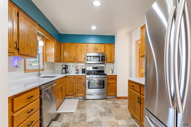 kitchen with a sink, stainless steel appliances, brown cabinetry, and light countertops