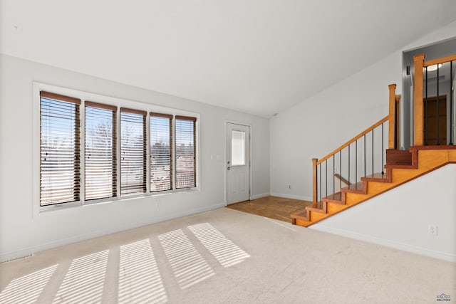 foyer entrance featuring baseboards, carpet floors, stairs, and vaulted ceiling