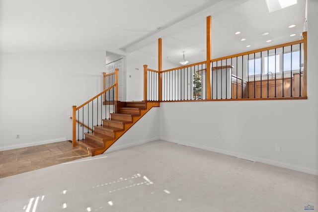 spare room featuring stairs, vaulted ceiling with skylight, baseboards, and carpet floors