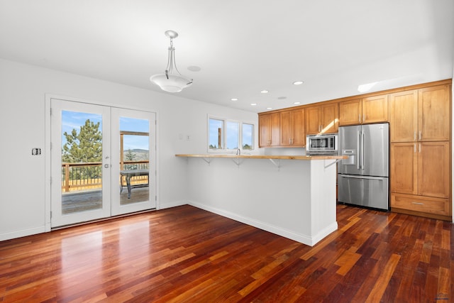 kitchen featuring dark wood-style floors, a breakfast bar, a peninsula, stainless steel appliances, and light countertops