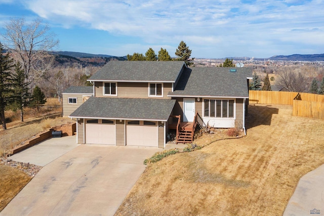 tri-level home featuring a mountain view, a shingled roof, driveway, and fence