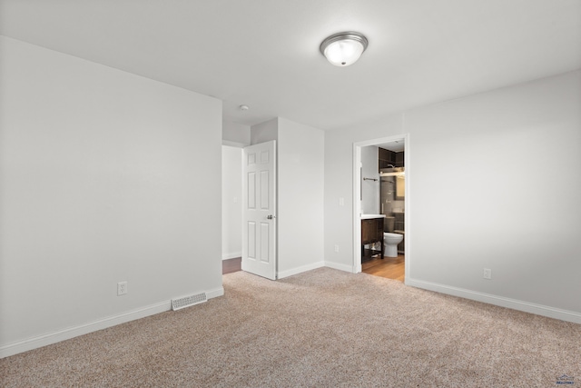 unfurnished bedroom featuring visible vents, carpet flooring, ensuite bath, and baseboards