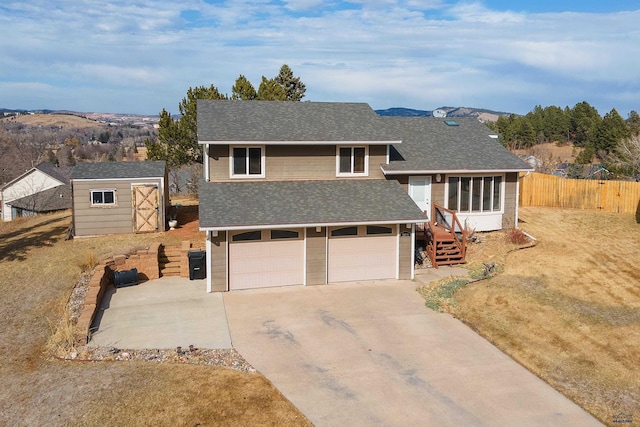 view of front of property with a storage unit, driveway, fence, an attached garage, and a shingled roof