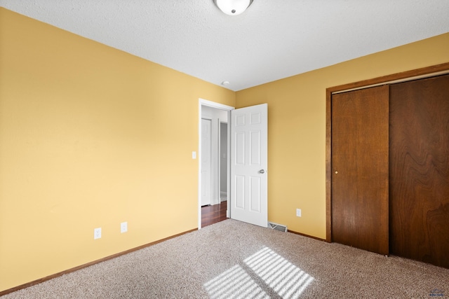 unfurnished bedroom featuring visible vents, a textured ceiling, a closet, carpet floors, and baseboards