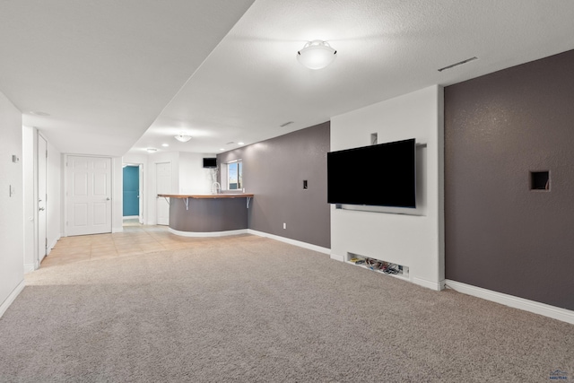 unfurnished living room featuring light carpet, visible vents, a textured ceiling, and baseboards