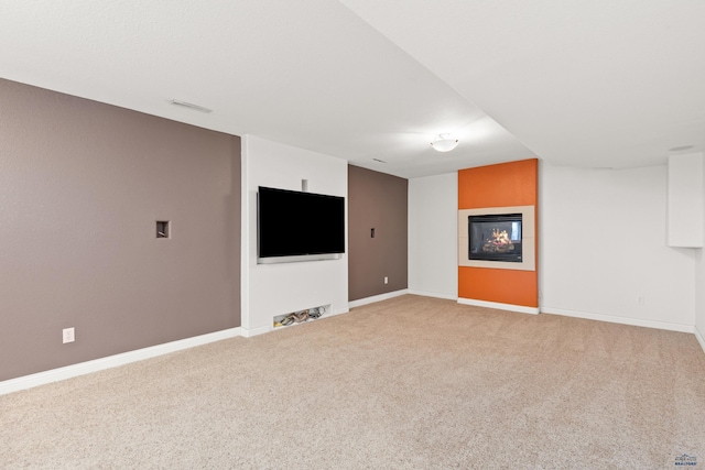 interior space featuring a glass covered fireplace, baseboards, visible vents, and light carpet