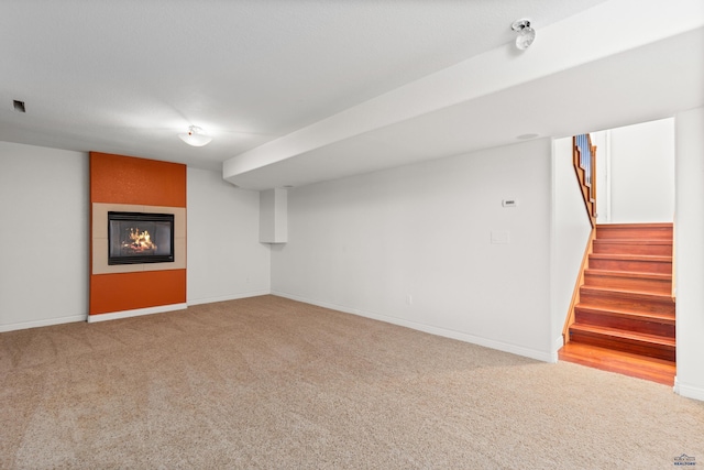 finished basement with stairway, baseboards, carpet, and a glass covered fireplace