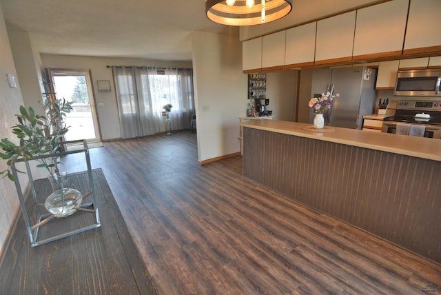 kitchen featuring baseboards, a peninsula, dark wood-style flooring, light countertops, and appliances with stainless steel finishes