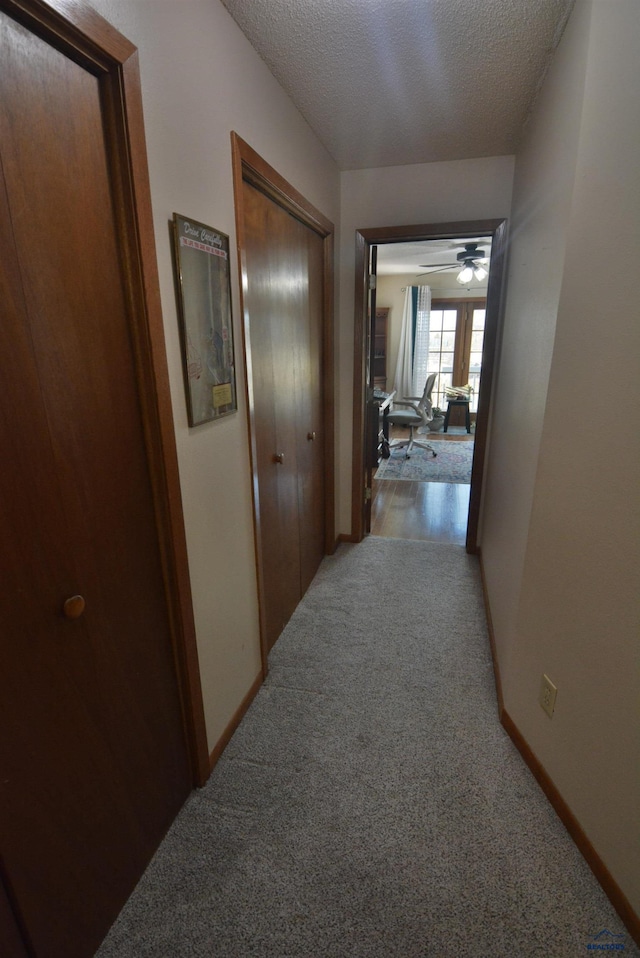 hallway featuring light carpet, baseboards, and a textured ceiling