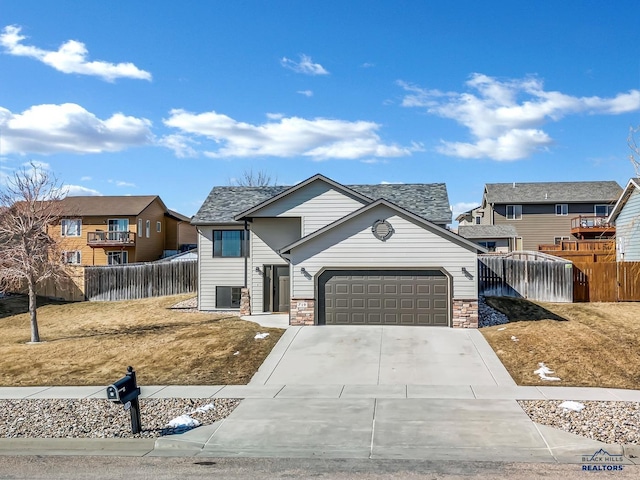 view of front of home with stone siding, an attached garage, driveway, and fence