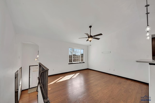 unfurnished living room with arched walkways, lofted ceiling, baseboards, and wood finished floors