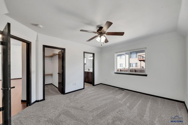 unfurnished bedroom featuring baseboards, ceiling fan, a spacious closet, carpet flooring, and connected bathroom