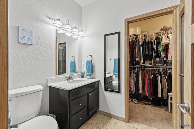 bathroom featuring toilet, vanity, a walk in closet, and baseboards