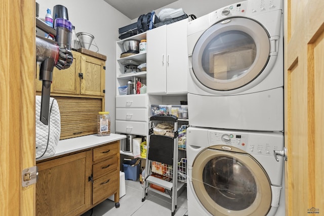 clothes washing area with light tile patterned floors, stacked washer / drying machine, and cabinet space