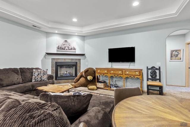 carpeted living room with visible vents, a tiled fireplace, a tray ceiling, recessed lighting, and arched walkways