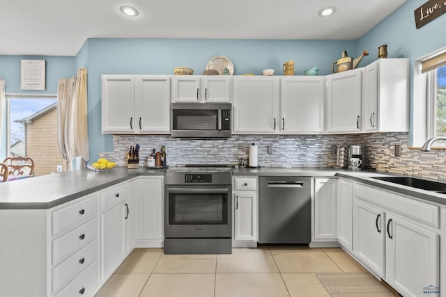 kitchen featuring light tile patterned floors, a peninsula, a sink, white cabinets, and appliances with stainless steel finishes