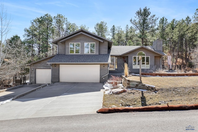 tri-level home featuring a garage, a chimney, driveway, and a shingled roof