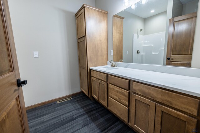 bathroom with vanity, wood finished floors, visible vents, baseboards, and a shower