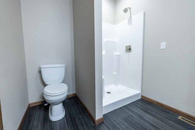 bathroom featuring wood finished floors, baseboards, visible vents, walk in shower, and toilet