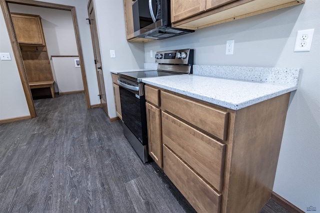 kitchen with brown cabinetry, light stone countertops, baseboards, dark wood-type flooring, and appliances with stainless steel finishes