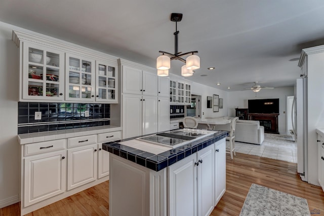 kitchen with tile countertops, a kitchen island, white cabinets, black electric stovetop, and open floor plan