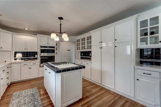 kitchen with stainless steel double oven, white cabinetry, a center island, and tile counters