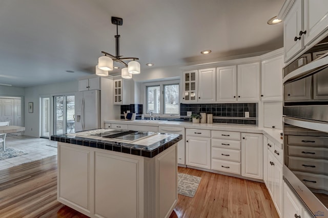 kitchen featuring tile countertops, a wealth of natural light, white refrigerator with ice dispenser, white cabinets, and black electric cooktop