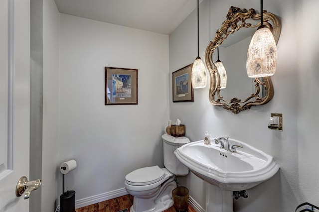 bathroom with toilet, wood finished floors, baseboards, and a sink