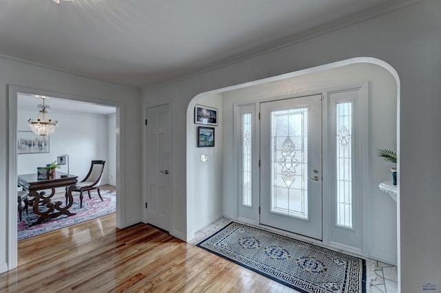 entryway with crown molding, baseboards, arched walkways, and light wood finished floors