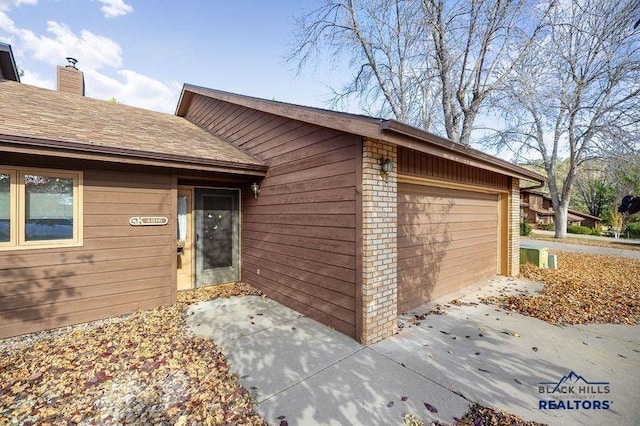 property entrance with a garage, a chimney, and a shingled roof