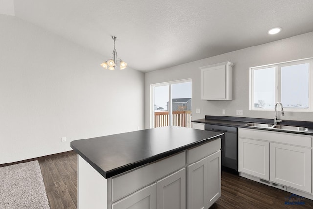 kitchen with a sink, vaulted ceiling, dark wood-type flooring, dishwasher, and dark countertops