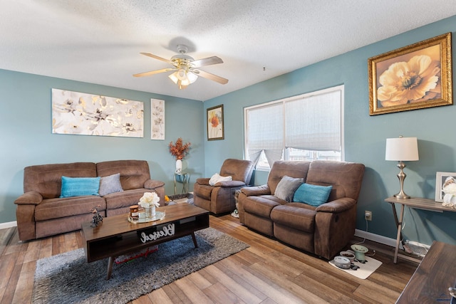 living room with a textured ceiling, a ceiling fan, baseboards, and wood finished floors