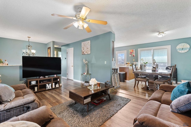 living area with baseboards, a textured ceiling, wood finished floors, and ceiling fan with notable chandelier